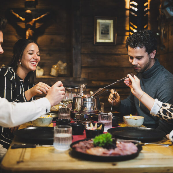 Gesellige Freundesgruppe am reichlich gedeckten Tisch mit zarter Fleischauswahl und hausgemachten Saucen beim Fondue Essen