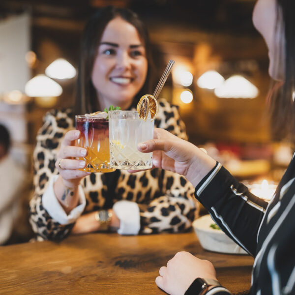 Zwei Damen mit leckeren Cocktails beim Anstoßen an der Bar